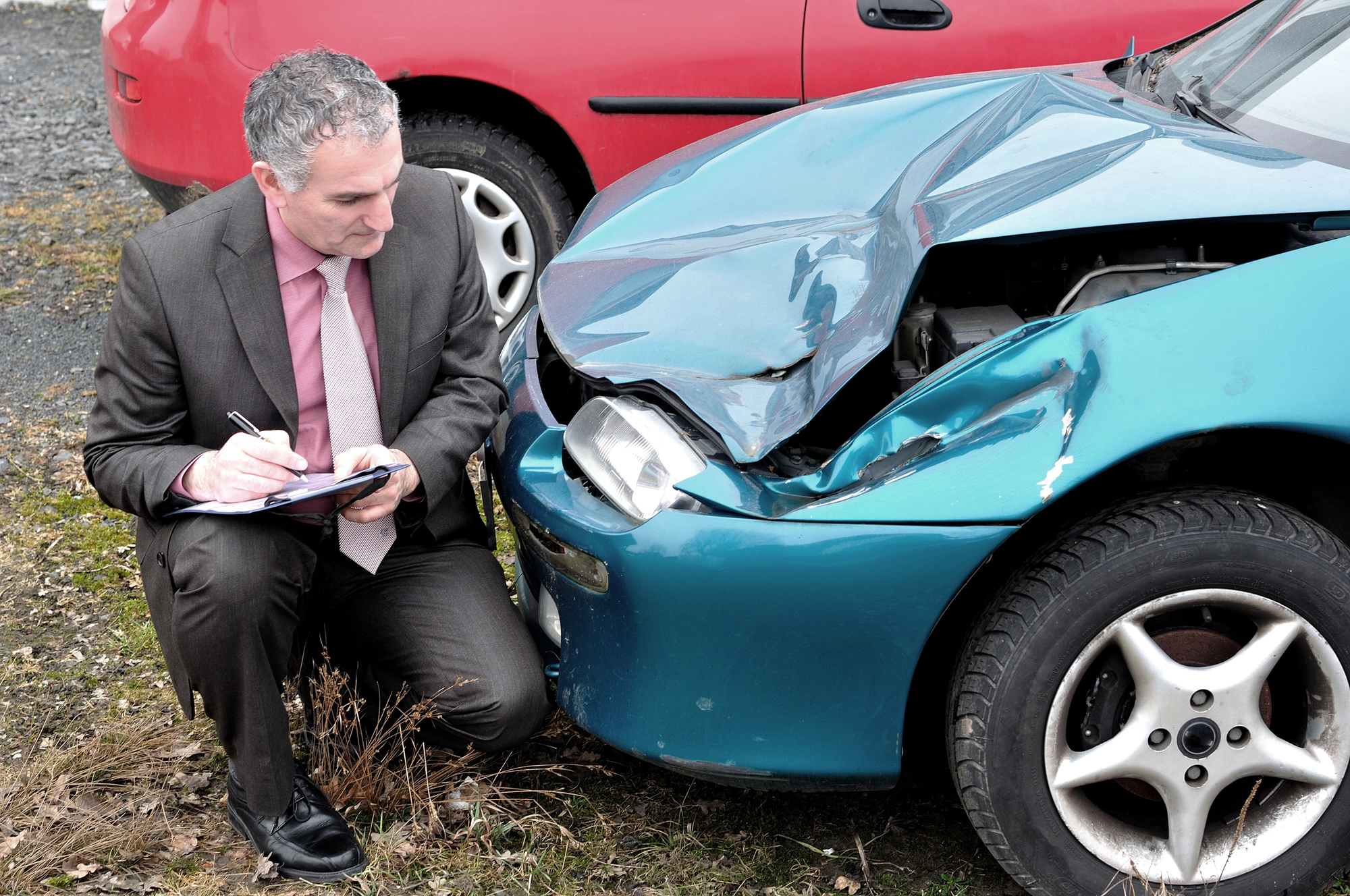 Insurance adjuster documenting front-end vehicle damage after a car accident, assessing impact severity and recording details for an auto insurance claim investigation.
