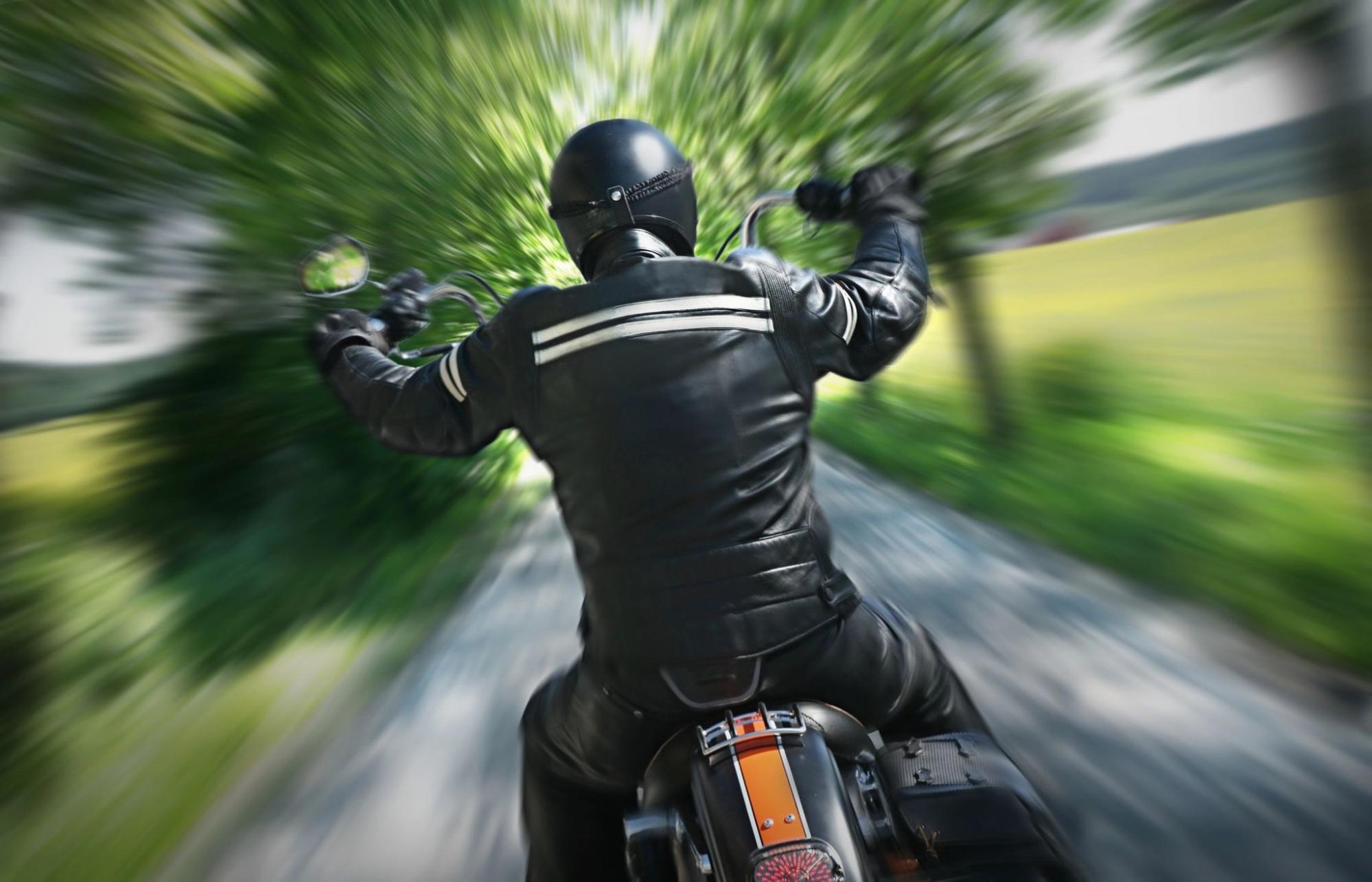 A motorcyclist in full leather gear rides at high speed on an open road, illustrating the importance of motorcycle helmet laws.