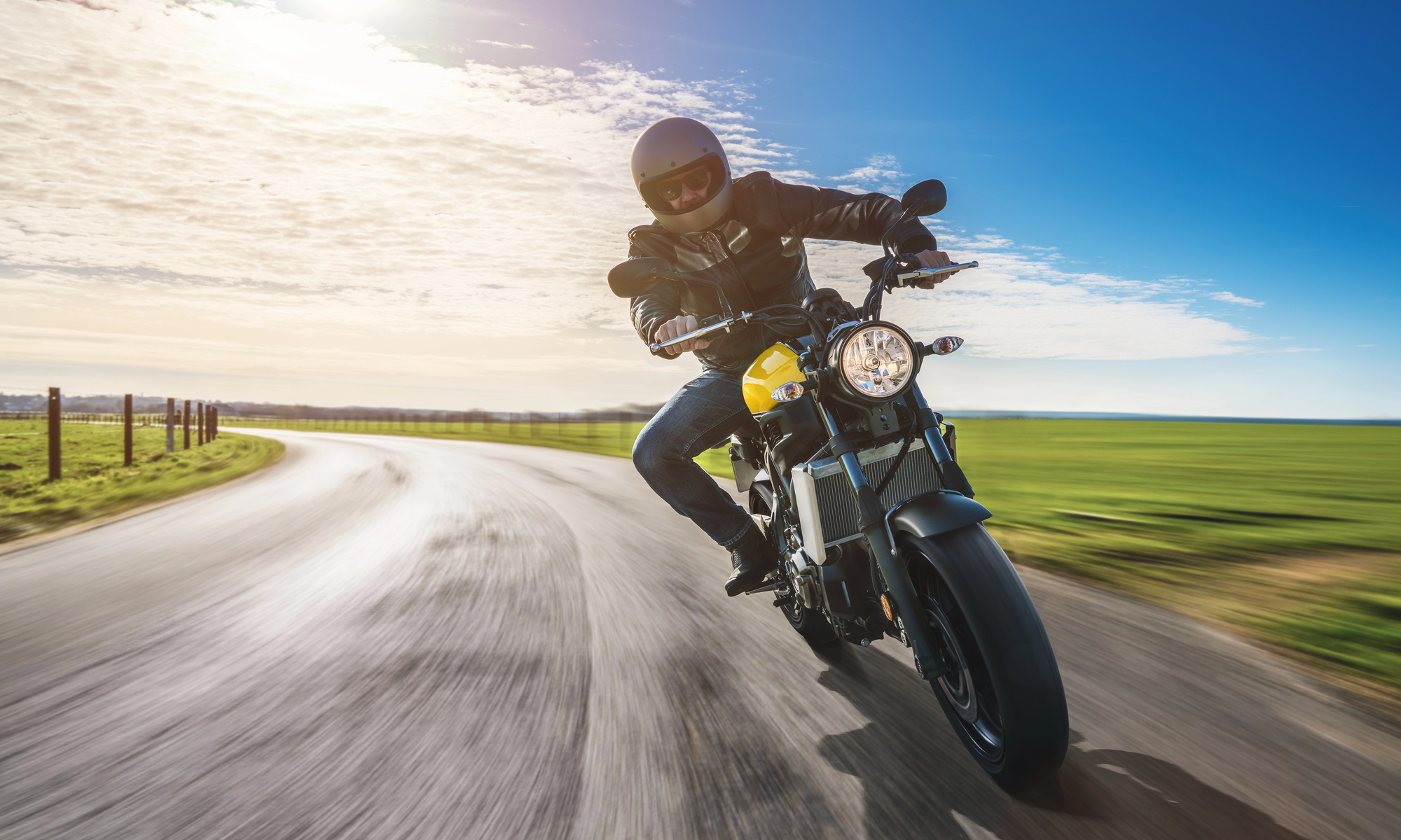A motorcycle rider in full gear leans into a curve on an open road, illustrating the speed and force involved in a pedestrian accident.