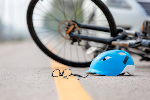 Damaged bicycle, cracked glasses, and helmet on the road, illustrating common injuries from bicycle accidents with vehicles.