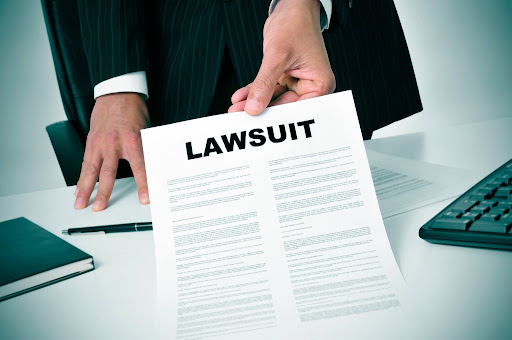 A businessman holds a document labeled "Lawsuit" at his desk, representing a personal injury or wrongful death lawsuit.