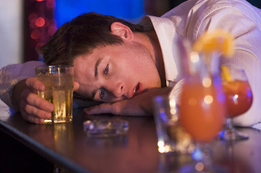 Man resting head on bar counter beside drinks, illustrating premises liability and negligent security risks.